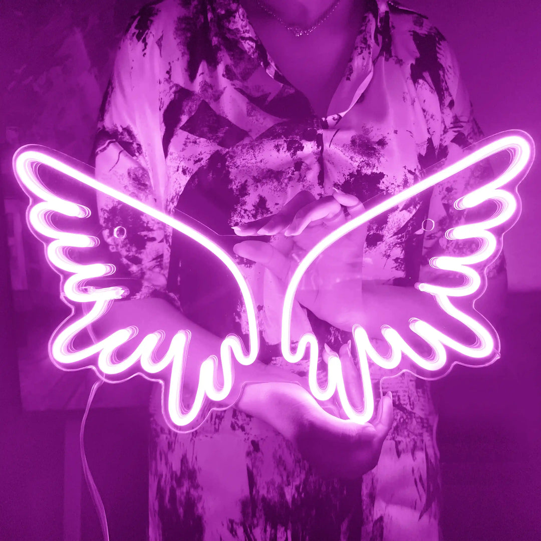 A girl holding a custom neon sign of pink color in the shape of angel wings | ManhattanNeons