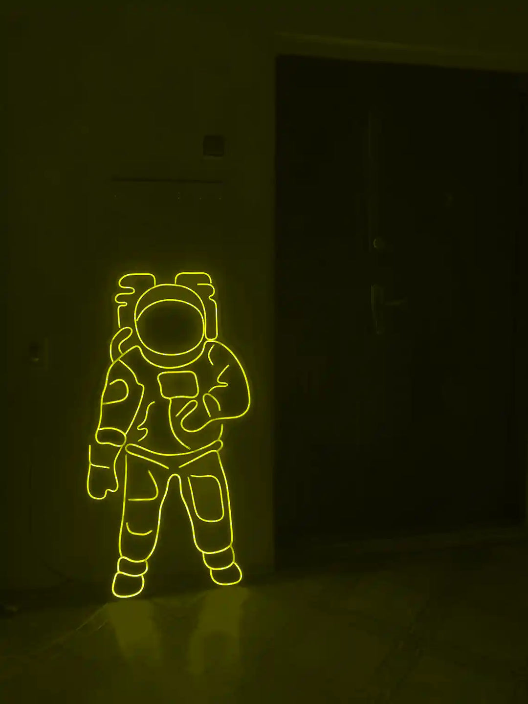 Yellow colored Astronaut LED Neon Sign placed on the floor beside a door - from manhattonneons.com.