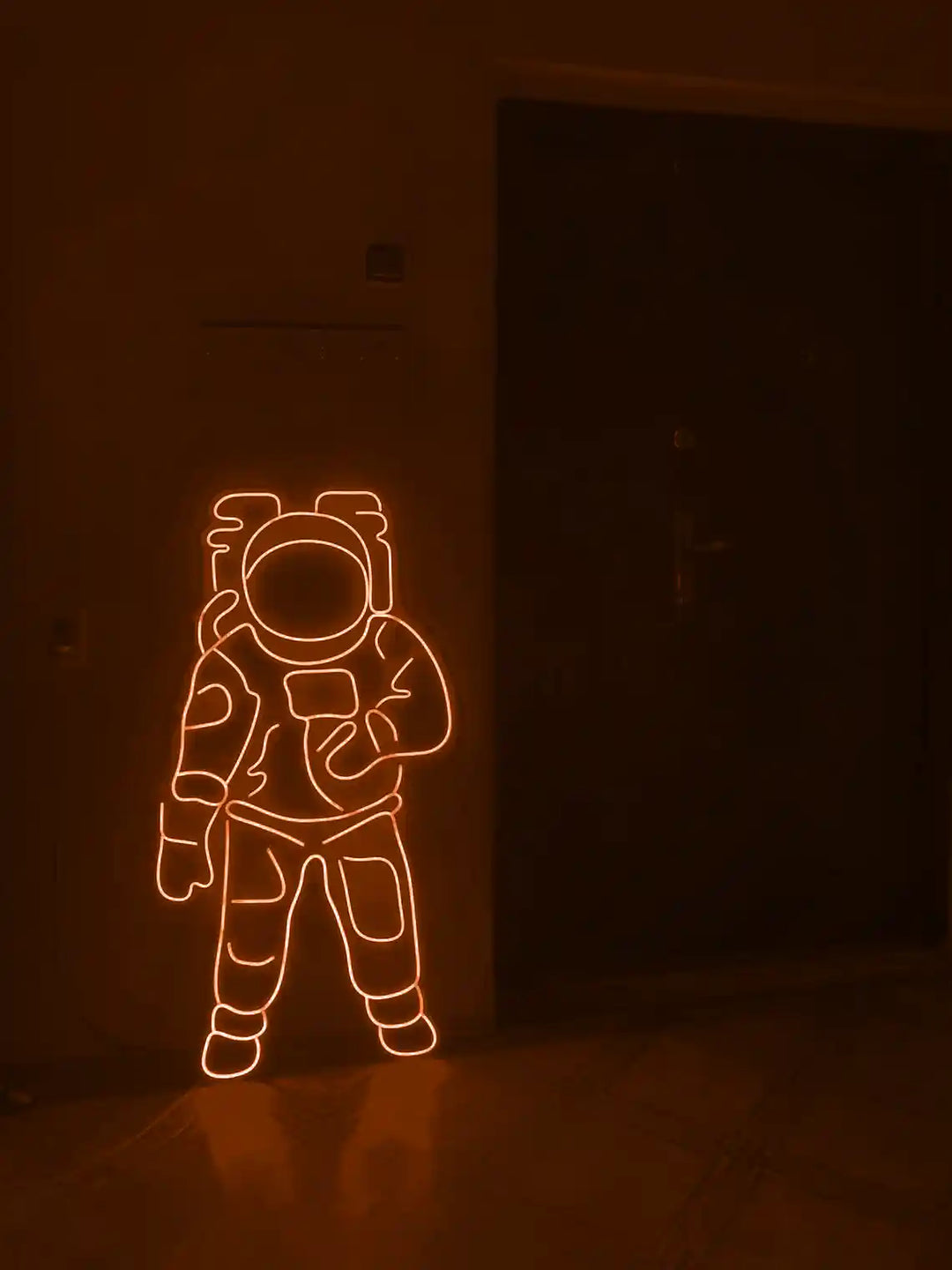 Orange colored Astronaut LED Neon Sign placed on the floor beside a door - from manhattonneons.com.